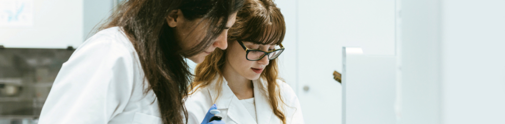 Two women in lab coats examining something in a lab.