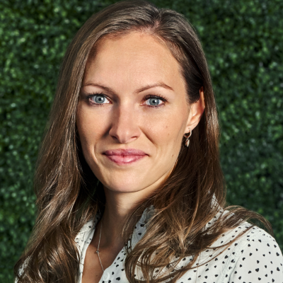 A woman wearing a polka dot shirt stands confidently in front of a vibrant green wall.