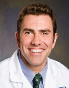 A smiling male doctor in a white coat and tie, working as a CRO.