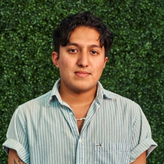 A young man in a striped shirt standing in front of a green wall.