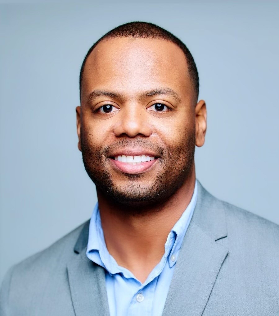 A black man attending the 14th Annual Summit, dressed in a gray suit and blue shirt.