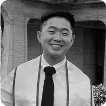 A man holding a vial while wearing a graduation gown.