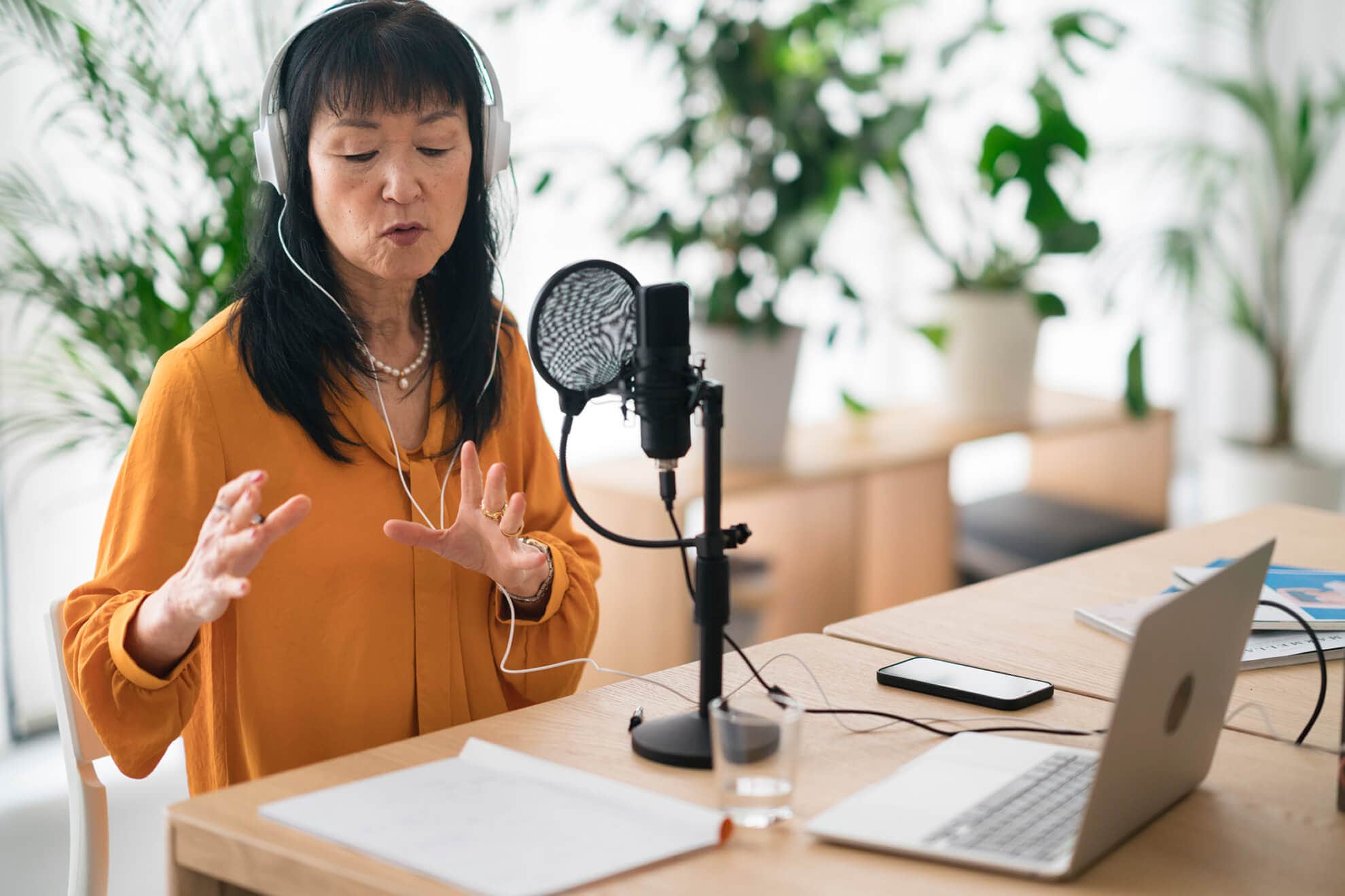 An Asian woman speaking into a microphone in front of a laptop while recording biotech podcasts.